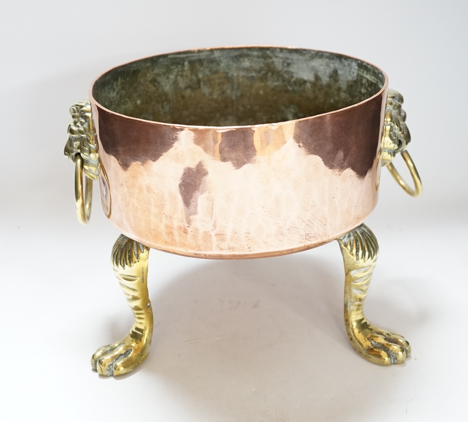 A heavy copper planter or cooking pot, with cast brass lion mask and ring handles, on brass claw feet, 20cm high